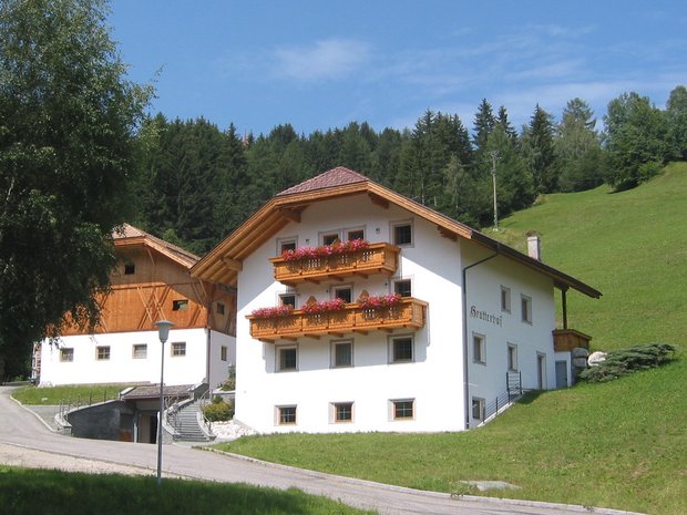 Le quattro strutture del nostro hotel in Val Pusteria a 4 stelle Casa colonica bianca tradizionale con balconi in legno e fiori in paesaggio montano verde