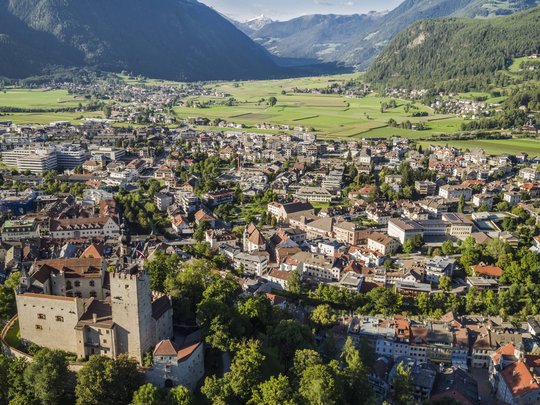 I dintorni del nostro hotel a 4 stelle in Val Pusteria Veduta aerea di una città con castello e montagne circostanti con cielo sereno