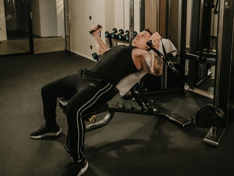 Baden im Pragser See? Hotel mit Pool? Brrr, ab in den Pool! Mann trainiert Brustmuskeln mit Kabelzug an Schrägbank im Fitnessstudio.