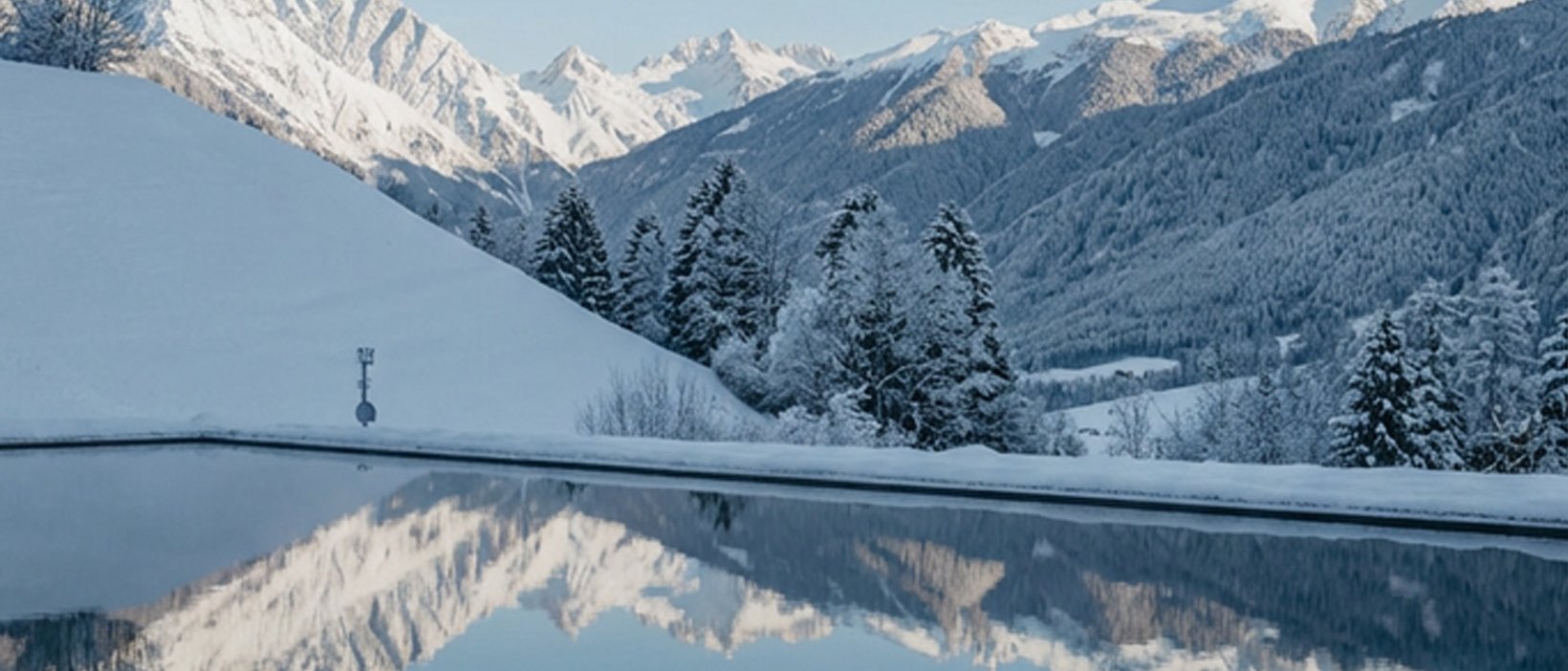Baden im Pragser See? Hotel mit Pool? Brrr, ab in den Pool! Schneebedeckte Berge spiegeln sich in einem ruhigen See unter blauem Himmel