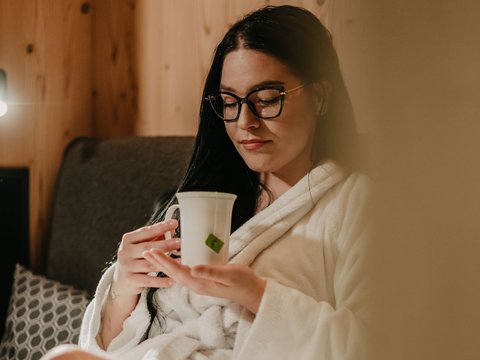 Vacanza da sogno: le offerte del nostro hotel in Val Pusteria Donna in accappatoio si rilassa con bevanda calda sul divano