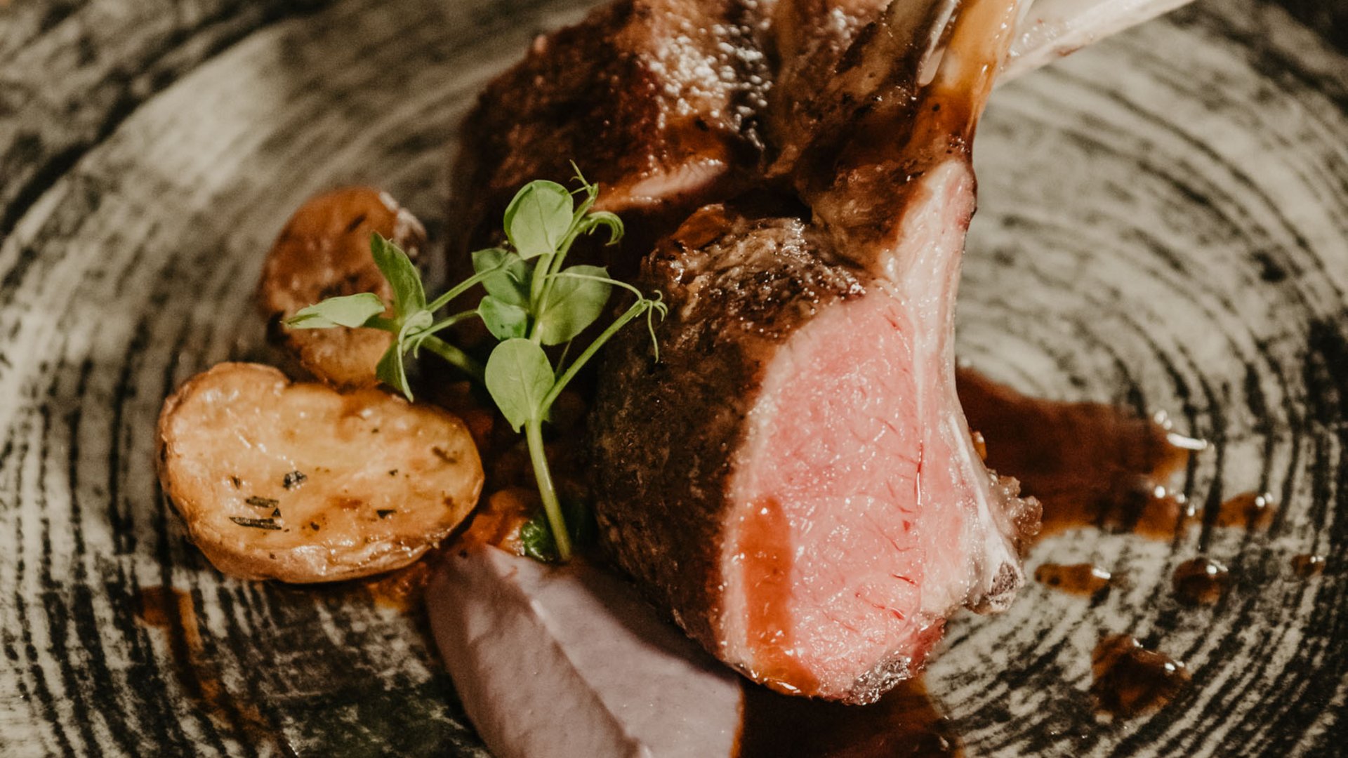 Cucina regionale nel nostro hotel in Val Pusteria a 4 stelle Costolette di agnello grigliate con patate e salsa su un piatto decorativo