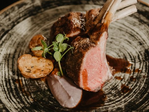 Traum-Dolomiten: Unterkunft mit Angeboten und Urlaubspaketen Gegrillte Lammkoteletts mit Kartoffeln und Sauce auf einem dekorativen Teller