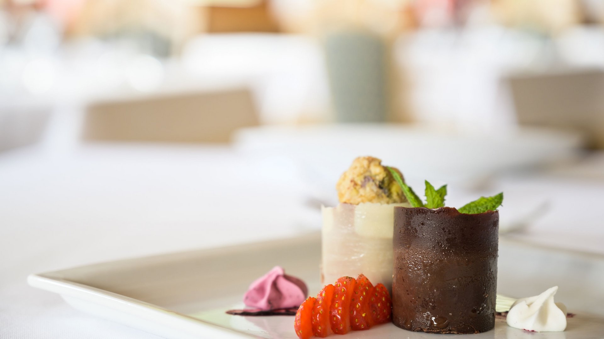 Cucina regionale nel nostro hotel in Val Pusteria a 4 stelle Dessert elegante con cioccolato, vaniglia, fragole e menta su piatto bianco