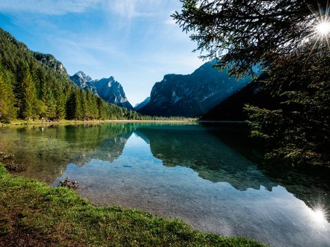 I dintorni del nostro hotel a 4 stelle in Val Pusteria Lago di montagna limpido con alberi di pino e luce solare