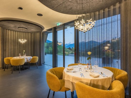 Willkommen in Olang: Hotel Christoph Elegantes Restaurant mit runden Tischen und gelben Stühlen mit Bergblick