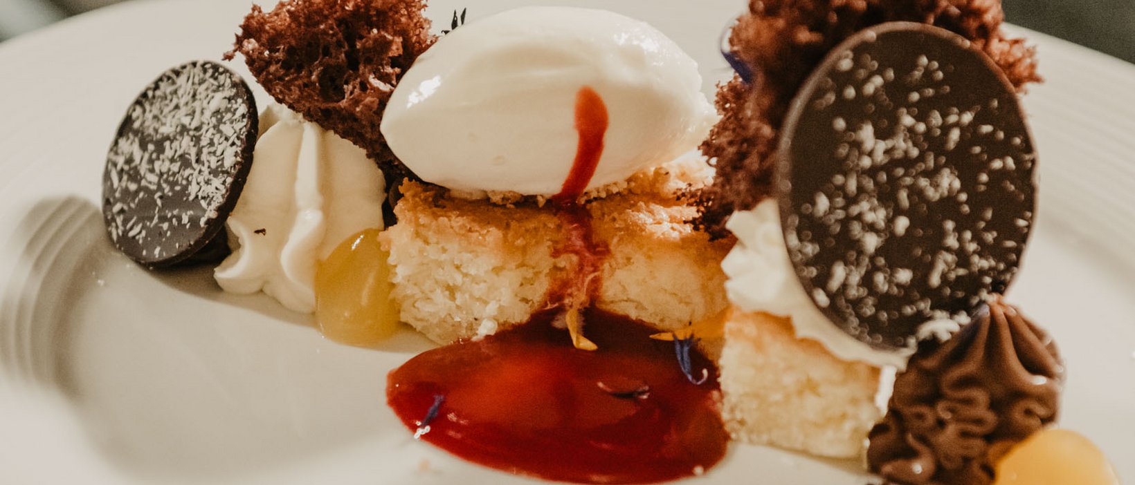 Wandern, Bergsteigen und Wellness: Kronplatz Kunstvoll angerichteter Nachtisch mit Schokolade, Sahne und Sauce auf weißem Teller