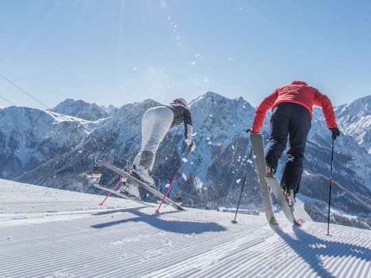 Novità dal nostro hotel al Plan de Corones Due sciatori scendono una pista innevata sotto il sole tra le montagne