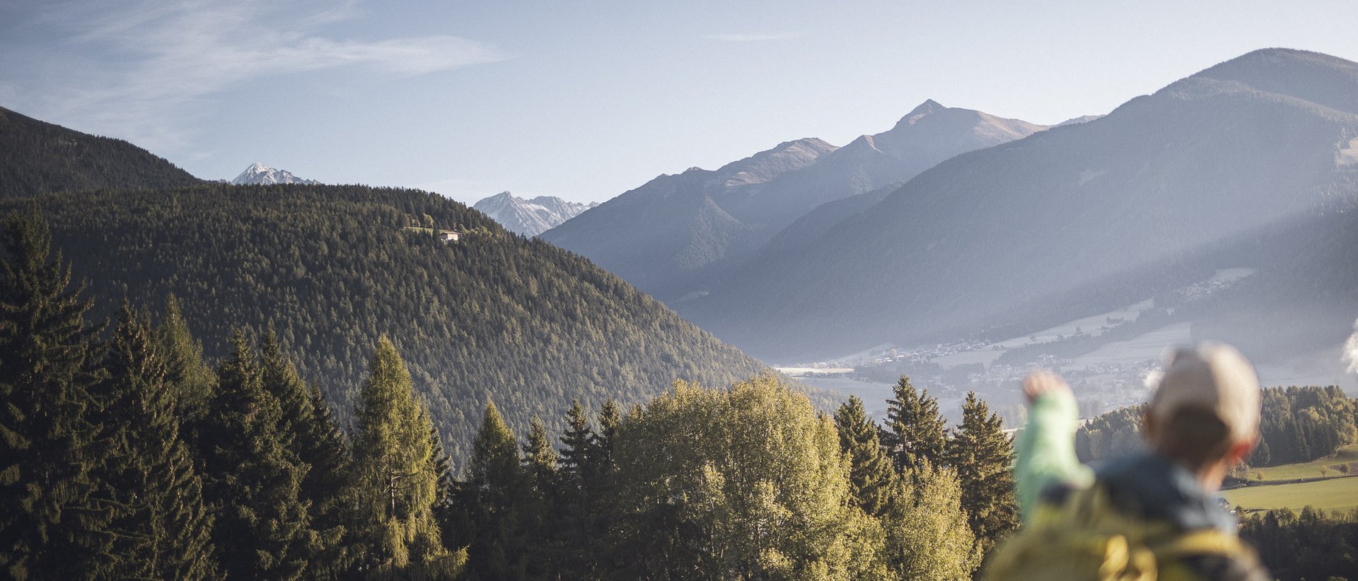 Wandern im Pustertal Wanderer zeigt auf bewaldete Berge und Tal bei klarem Himmel