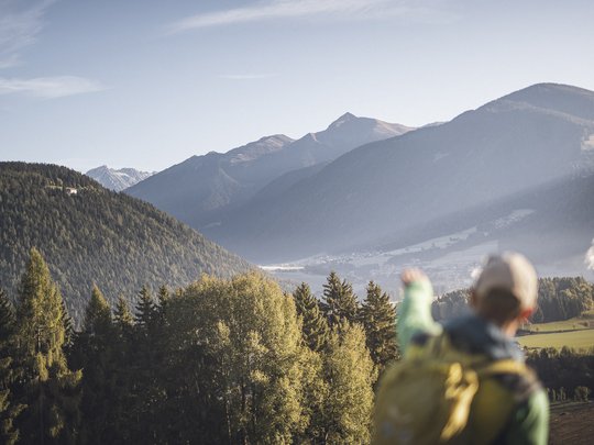 Neuigkeiten unseres Hotels nahe dem Pragser Wildsee Wanderer zeigt auf bewaldete Berge und Tal bei klarem Himmel