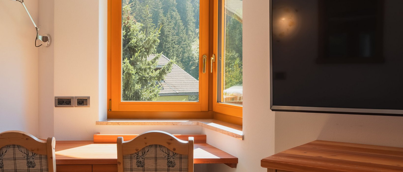 Bewertungen unseres Hotels im Pustertal mit 4 Sternen Holzarbeitsplatz mit Fensterblick auf grüne Berge und Fernseher an der Wand