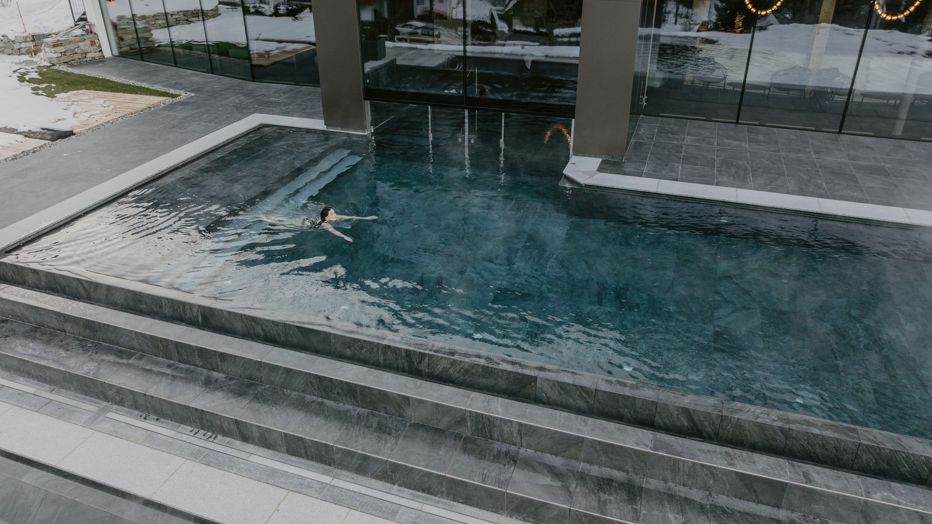 Concedetevi una pausa Persona che nuota in piscina esterna moderna accanto a edificio con neve invernale.