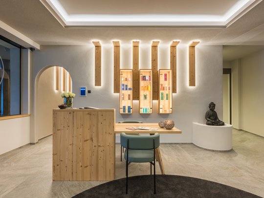 Willkommen in Olang: Hotel Christoph Empfangsbereich mit Holztheke, Stühlen, dekorativer Wandbeleuchtung und Buddha-Statue