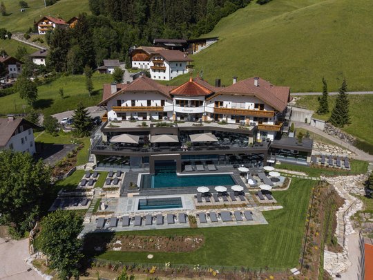 Una giornata di relax Veduta aerea di un hotel con piscina esterna e lettini in un paesaggio montano verde