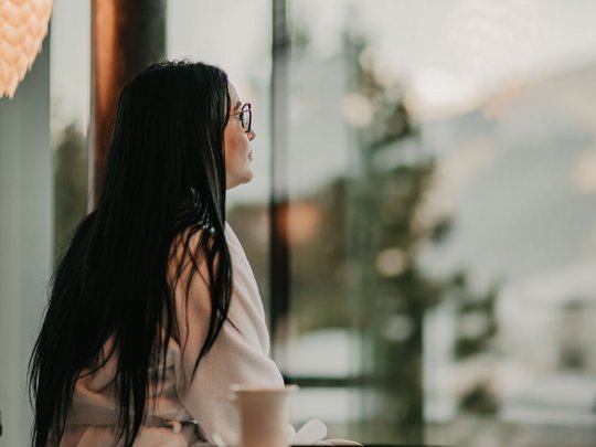 Una giornata di relax Donna in accappatoio seduta sul letto guarda fuori dalla grande finestra