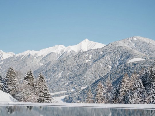 Le novità del nostro hotel a 4 stelle tra le Dolomiti Montagne e alberi innevati si riflettono in un lago calmo sotto un cielo azzurro chiaro