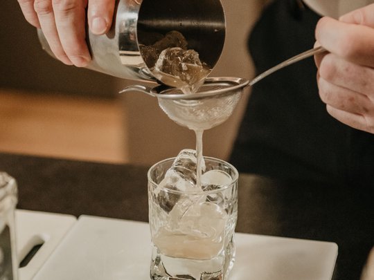 Concedetevi una pausa Barista versa cocktail attraverso un colino in un bicchiere con ghiaccio