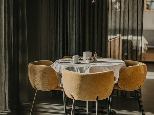Le novità del nostro hotel a 4 stelle tra le Dolomiti Tavolo rotondo con tovaglia bianca e quattro sedie marroni davanti a tende scure
