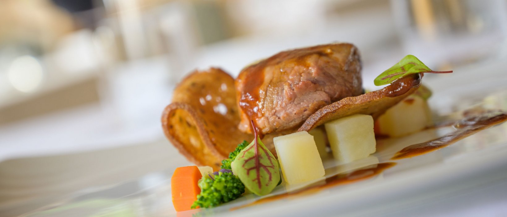 Sustainable 4-star hotel in the Dolomites Gourmet dish with tender meat, vegetables, and sauce on a white plate