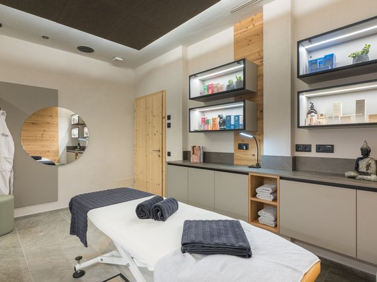 4-Sterne-Hotel am Kronplatz: Ihr perfektes Urlaubszuhause Modernes Massagestudio mit Behandlungsliege und dekorativen Regalen