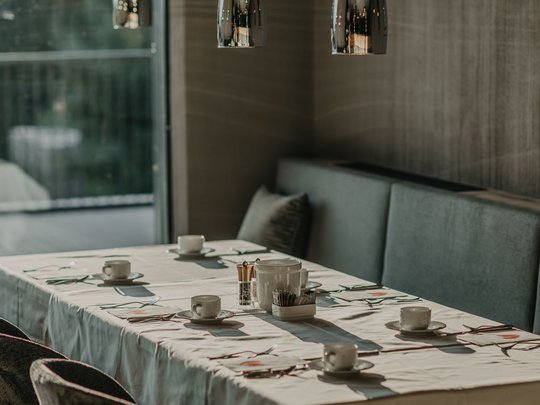 Le novità del nostro hotel a 4 stelle tra le Dolomiti Un tavolo apparecchiato con tazze sotto lampade a sospensione moderne in un ristorante.