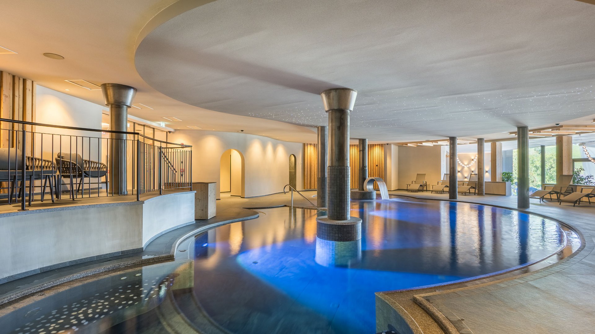 Willkommen in Olang: Hotel Christoph Innenpool mit blauem Licht, Säulen und Liegestühlen in modernem Spa-Bereich