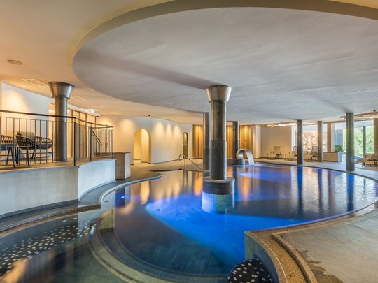 Le novità del nostro hotel a 4 stelle tra le Dolomiti Piscina interna con luce blu, colonne e sedie a sdraio in centro benessere moderno