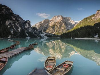 Vorbei am Pragser Wildsee zum Hotel: Ihr Weg in den Urlaub Holzboote auf ruhigem Bergsee mit Spiegelung und bewaldeten Bergen