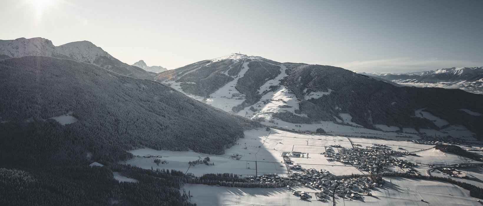 Der Kronplatz aus nächster Nähe: Ihr Aktivhotel in Südtirol Verschneites Tal mit Dorf und Bergen bei Sonnenlicht