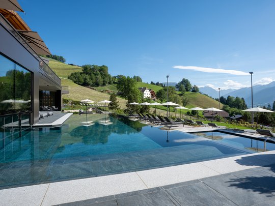 Hotel al Plan de Corones con spa: vacanza à la Christoph Piscina a sfioro con lettini e ombrelloni davanti a colline verdi e montagne