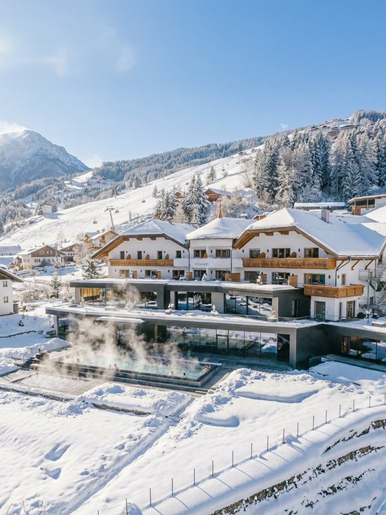 4-Sterne-Hotel am Kronplatz: Ihr perfektes Urlaubszuhause Hotel mit beheiztem Außenpool in verschneiter Berglandschaft bei sonnigem Winterwetter