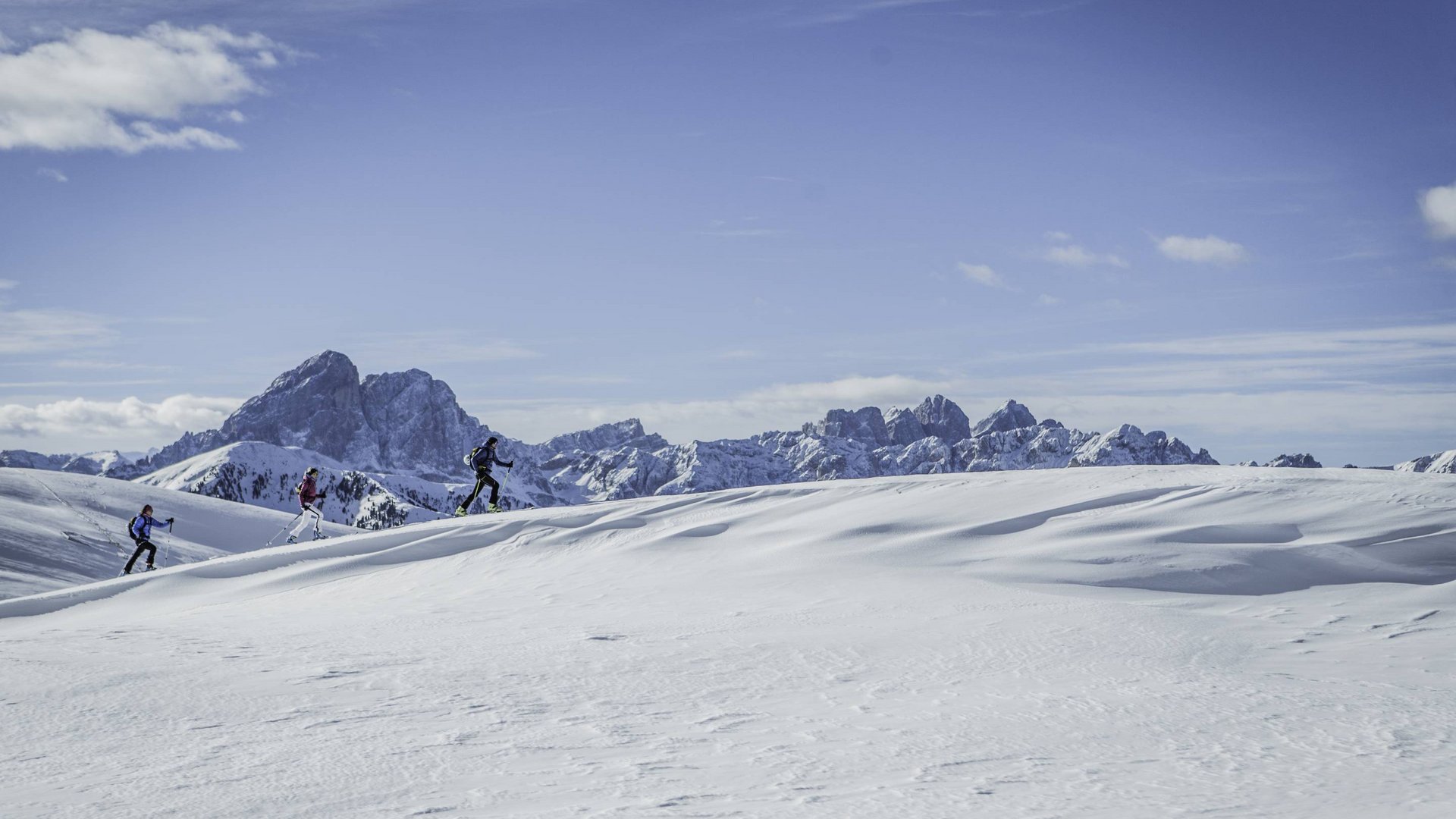 Attività invernali all’Hotel Christoph sulle Dolomiti Tre escursionisti con sci attraversano colline innevate con montagne sullo sfondo