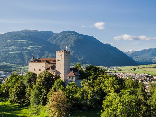 Neuigkeiten unseres Hotels nahe dem Pragser Wildsee Burg auf bewaldetem Hügel mit Bergen und Stadt im Hintergrund