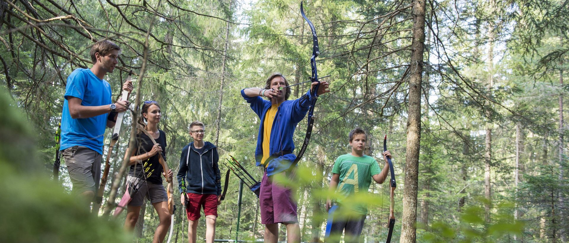 Corso di tiro con l’arco Gruppo di cinque persone che praticano il tiro con l'arco in un bosco