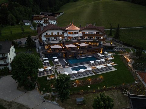 Unabhängiger Urlaub: Ihre Ferienwohnung in Olang Abendaufnahme eines beleuchteten Hotels mit Pool und Sonnenschirmen in den Bergen