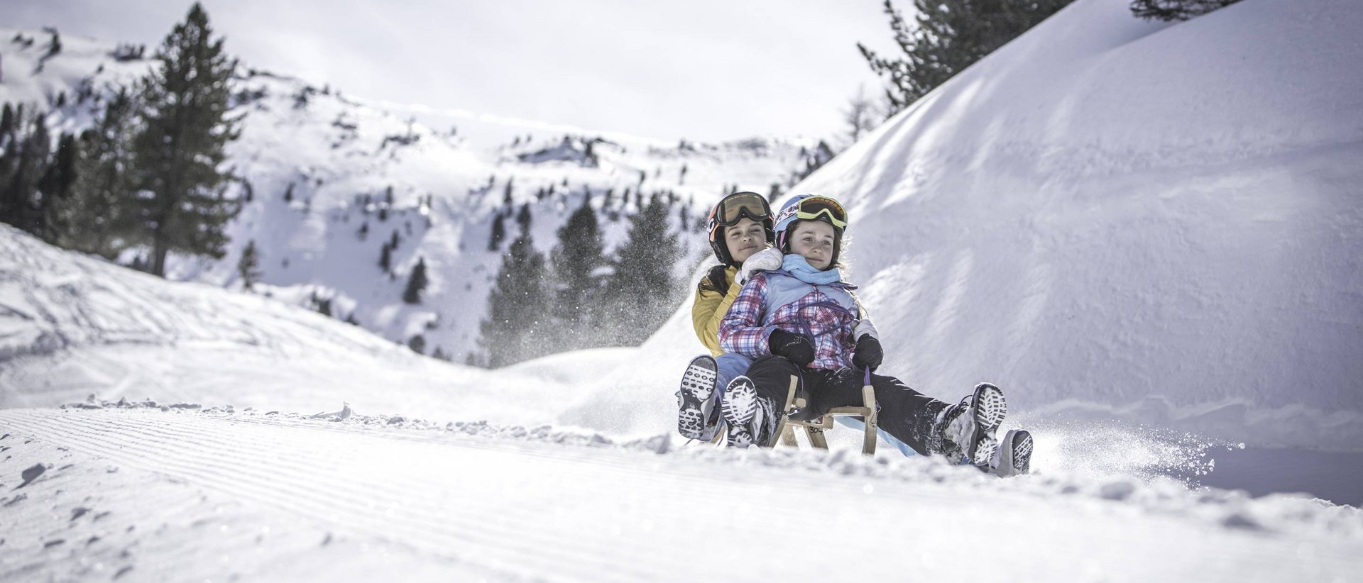 Rodelspaß für Groß und Klein: Rodelweg Brunst Zwei Kinder rodeln zusammen auf einem Schneehang im Winter
