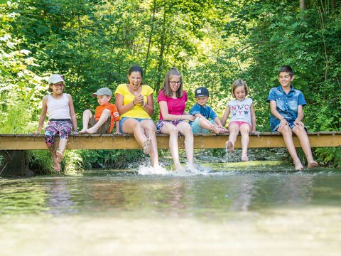 Massaggi nel nostro hotel benessere sulle Dolomiti Bambini seduti su un ponte che giocano con i piedi nell'acqua