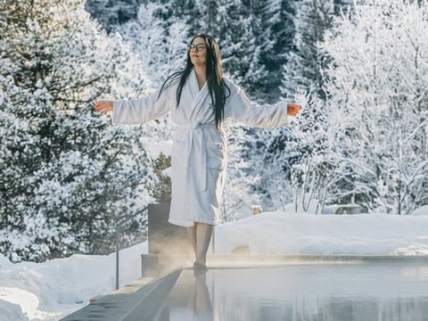 A swim in Lago di Braies? A hotel with a pool? Let’s go for a dip! Woman in bathrobe by heated pool in snowy winter forest