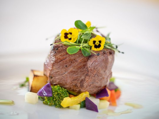 Regionale, alpine Küche im Hotel am Kronplatz in Südtirol Gourmet-Rinderfilet mit buntem Gemüse und essbaren gelben Blüten