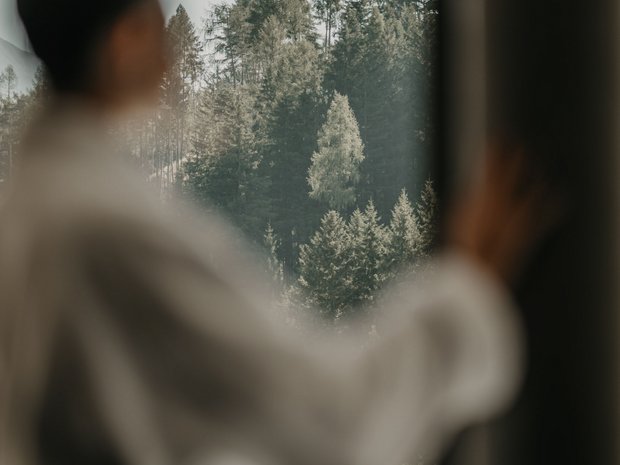 Sustainable 4-star hotel in the Dolomites Blurred person looking at forested hill through a window