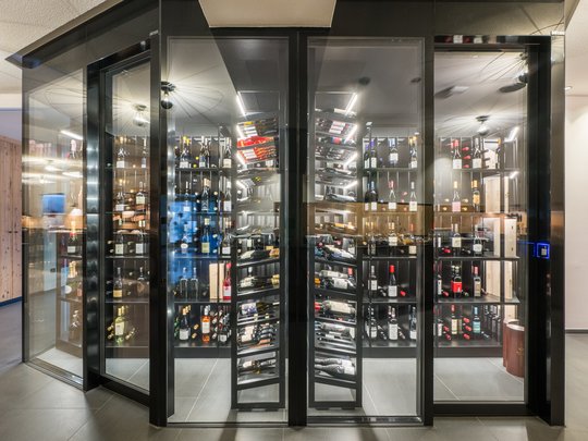 Willkommen in Olang: Hotel Christoph Moderner Weinkeller mit Glasrahmen und Weinflaschen auf Regalen
