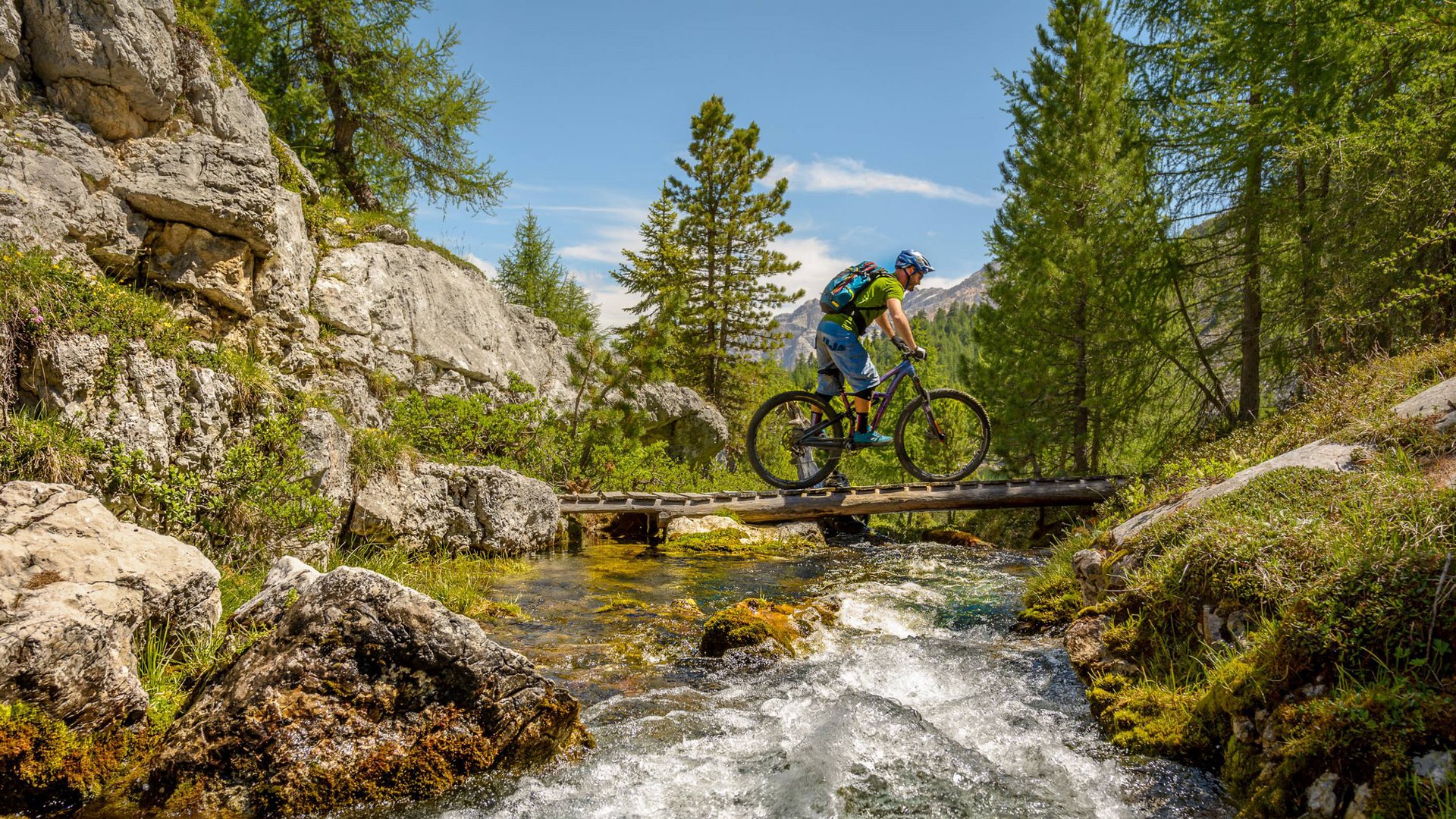 Unvergesslicher Skiurlaub am Kronplatz Mountainbiker überquert eine Brücke über einen Bach in den Bergen