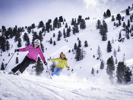Unforgettable skiing holiday on Plan de Corones/Kronplatz Two skiers in colorful outfits skiing down a snowy slope