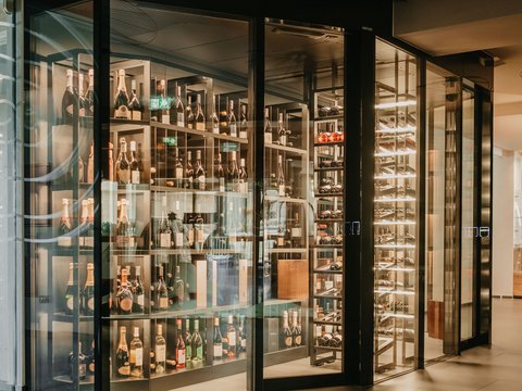 Family hotel a Valdaora: la famiglia Lanz Cantina moderna con pareti di vetro e scaffali illuminati pieni di bottiglie di vino