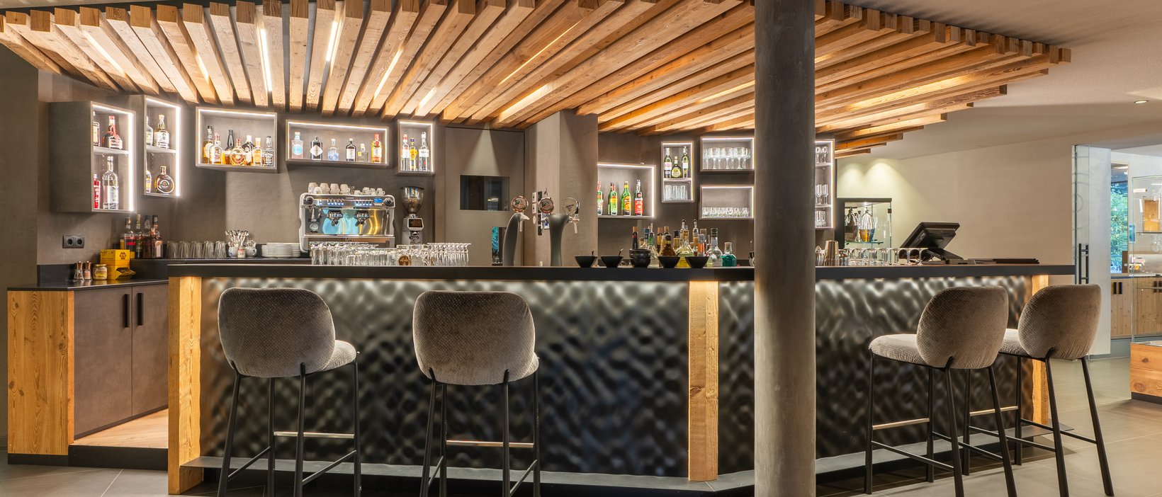 The four buildings of our accommodation in Val Pusteria/Pustertal Modern hotel bar area with illuminated wood design and tall bar stools