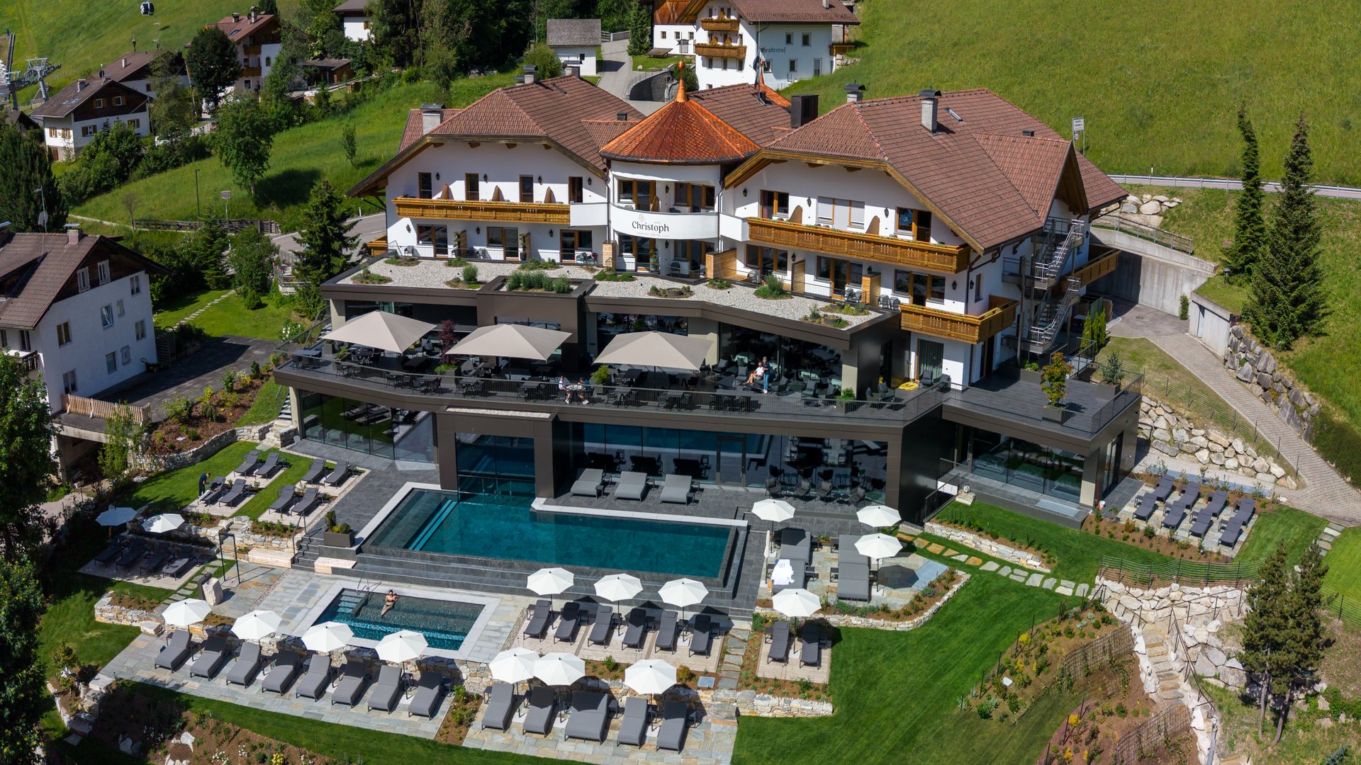 Willkommen in Olang: Hotel Christoph Hotel mit Pool und Sonnenschirmen in den Bergen bei klarem Himmel
