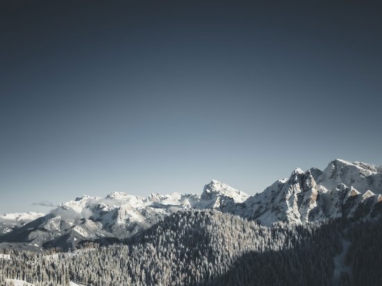 A warm welcome to our hotel in Olang, at Plan de Corones/Kronplatz Snow-covered mountain peaks and forest under clear sky