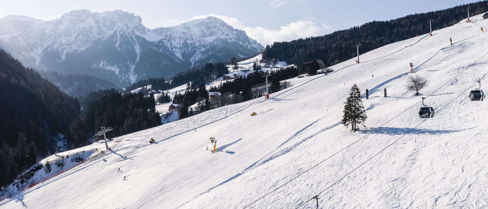 Escursioni invernali in Val Pusteria Pista da sci innevata con cabine della funivia e montagne sullo sfondo