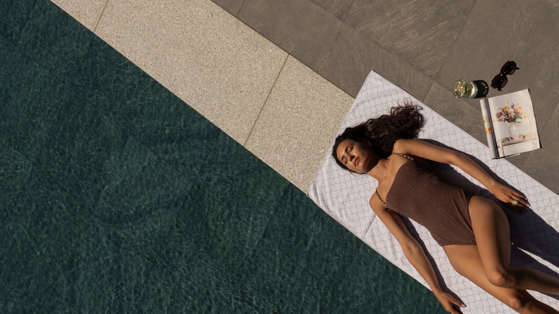 Concedetevi una pausa Donna sdraiata su asciugamano accanto alla piscina con libro, bevanda e occhiali da sole