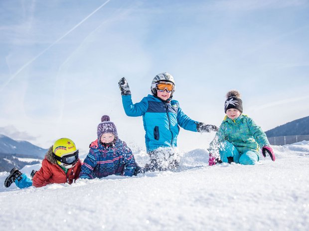 Sustainable 4-star hotel in the Dolomites Four children playing joyfully in the snow with winter clothes and helmet